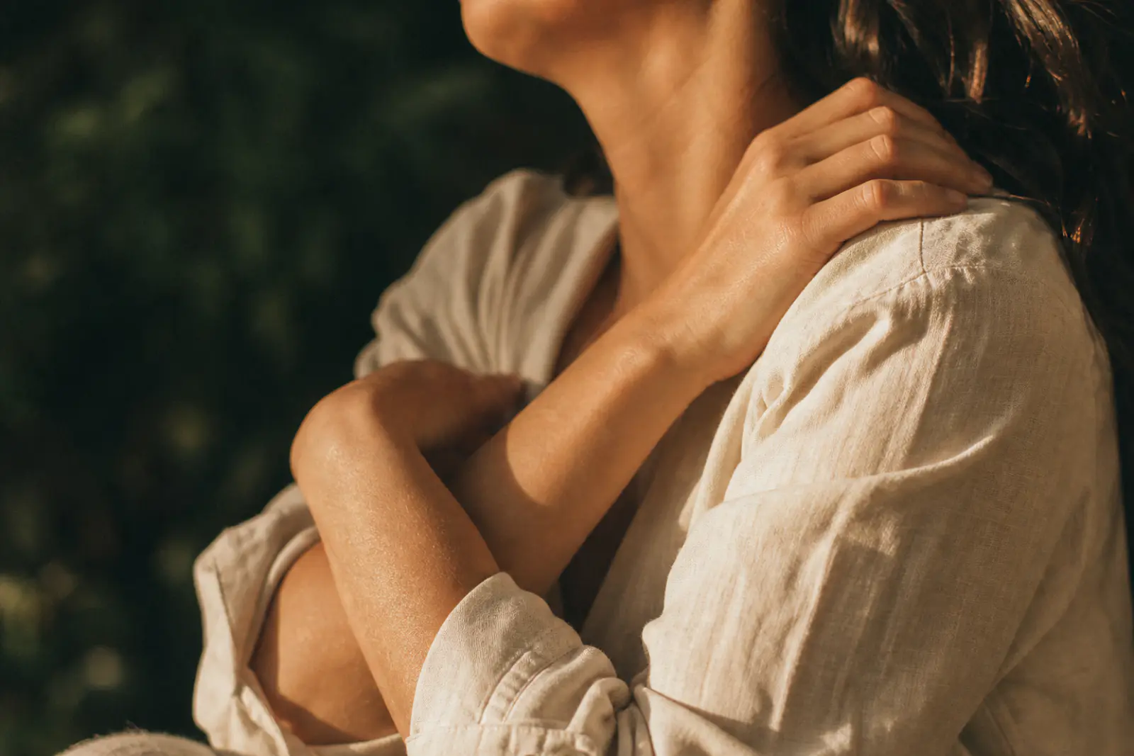 Mulher em luz natural, ombros relaxados, em gesto de acolhimento do próprio corpo